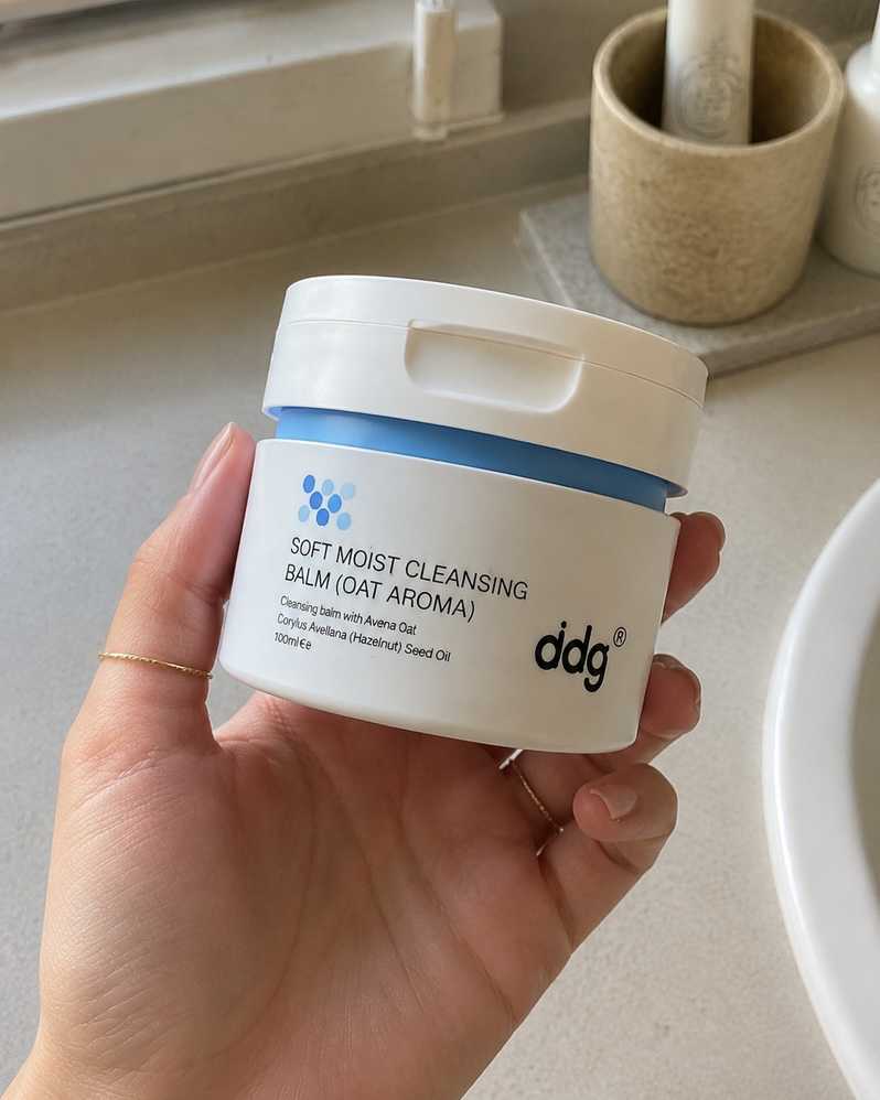 Hand holding an authentic ddg oat cleansing balm jar in a real bathroom setting
