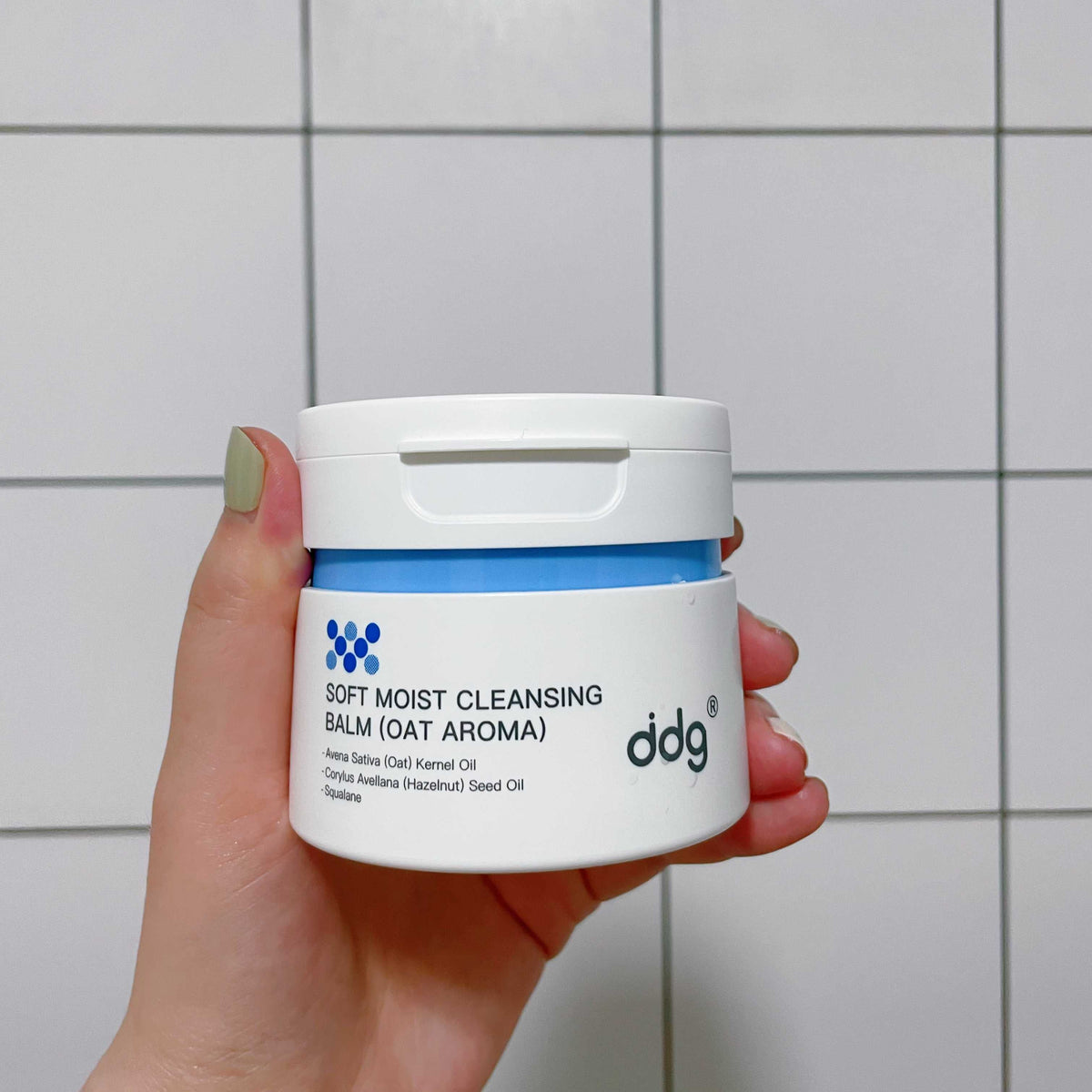 Hand holding an authentic ddg oat cleansing balm jar with the full product label and trademark visible
