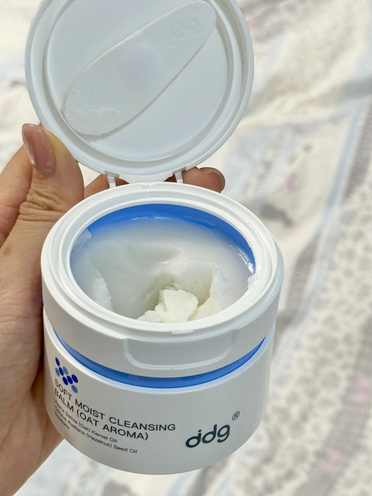 Authentic open ddg oat cleansing balm jar held in daylight with the full product label visible